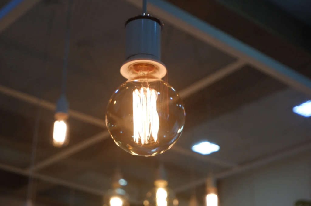 Warm glowing LED filament light bulb suspended from ceiling in modern home interior